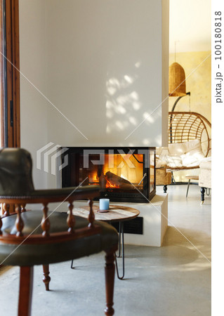 Cup of hot drink on table, warm fireplace with armchair in front and natural light from window 100180818