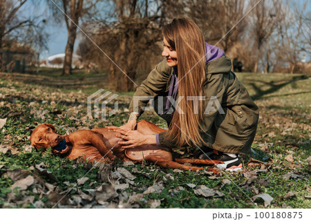 Woman Petting Vizsla Dog Lying in Park 100180875