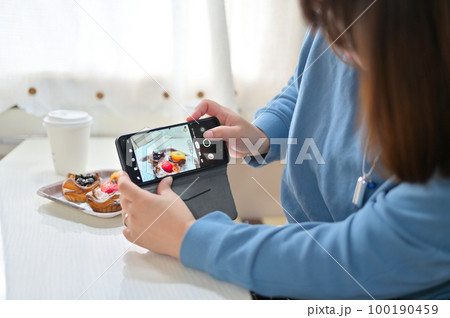 スマホでフルーツタルトを撮影する女性 100190459