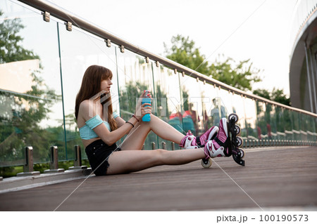 Skater girl sitting on bridge opens drink bottle 100190573