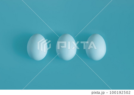 Three White chicken eggs on a blue background in the center. Three White chicken eggs on a blue background in the center. 100192502
