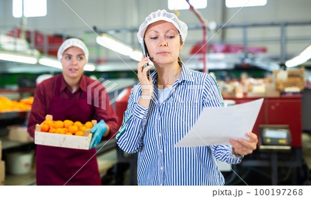 Fruit sorting factory forewoman with papers talking on phone 100197268