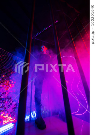 Caucasian woman in neon studio behind steel bars.  100201640