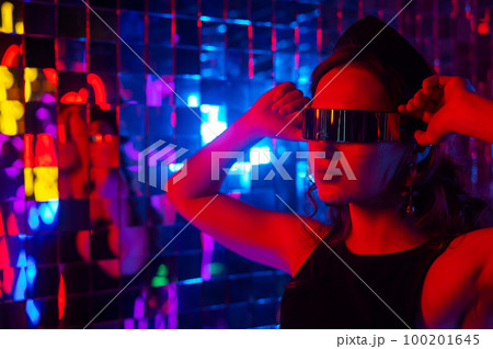 Close-up portrait of a caucasian woman in sunglasses in neon light against a mirror wall.  100201645