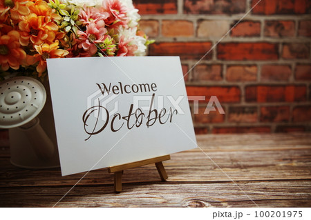 Welcome October text with flower bouquet decoration on wooden and old brick wall background 100201975