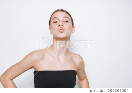 Beauty portrait of funny young girl with fresh skin tone showing kiss on white background isolated 100202304
