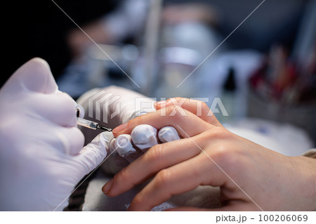 A beautician paints the nail of a client's ring finger A beautician paints the nail of a client's ring finger 100206069