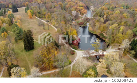 Beautiful landscape view of autumn park with lakes with swans, trees with yellow red green leaves, meadow, architecture, waterfall and people walking along dirt paths on autumn day. Natural background Beautiful landscape view of autumn park with lakes with swans, trees with yellow red green leaves, meadow, architecture, waterfall and people walking along dirt paths on autumn day. Natural background 100208425