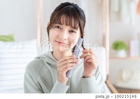 ヘアアイロンを使う若い女性 100215149