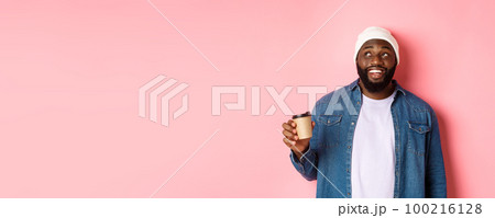 Handsome modern Black man drinking takeaway coffee, smiling and looking satisfied at camera, standing over pink background 100216128