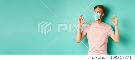 Covid-19, pandemic and lifestyle concept. Cheerful redhead man in medical mask showing okay signs in approval, like and praise product, looking left at copy space 100217771