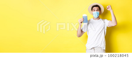 Concept of covid-19, travelling and quarantine. Happy man tourist in medical mask celebrating, showing passport with tickets for vacation and rejoicing, travel during coronavirus Concept of covid-19, travelling and quarantine. Happy man tourist in medical mask celebrating, showing passport with tickets for vacation and rejoicing, travel during coronavirus 100218045