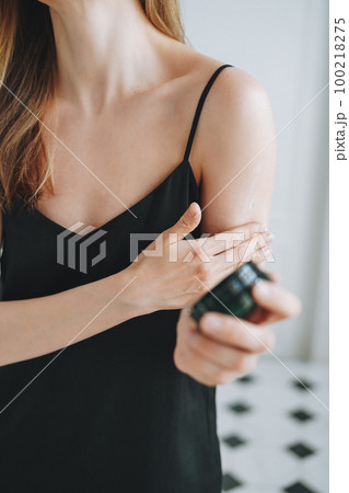 Young woman in black dress put day moisturizer body cream on clean fresh skin in bathroom at home 100218275