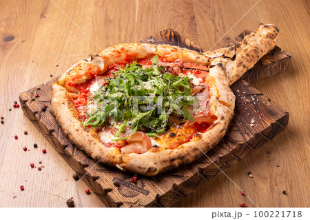 Oven baked pizza with mozzarella cheese, dried ham, tomatoes, balsamic vinegar and arugula 100221718