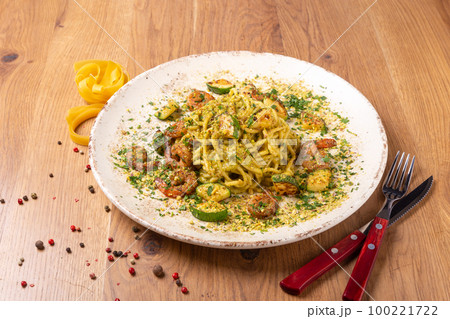Spaghetti Pesto with shrimps and zucchini served on wooden table, side view. 100221722