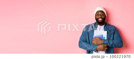 Image of adult Black man holding notebooks and smiling, studying at courses, standing over pink background 100221970