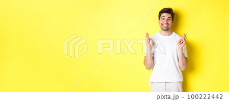 Hopeful smiling man holding fingers crossed, making wish or praying, standing over yellow background Hopeful smiling man holding fingers crossed, making wish or praying, standing over yellow background 100222442