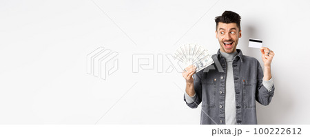 Excited guy holding plastic credit card and dollar bills, standing amused on white background Excited guy holding plastic credit card and dollar bills, standing amused on white background 100222612