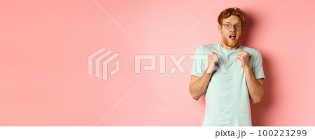 Portrait of scared redhead guy in glasses staring startled at camera, press hands to body and scream of fear, standing over pink background Portrait of scared redhead guy in glasses staring startled at camera, press hands to body and scream of fear, standing over pink background 100223299