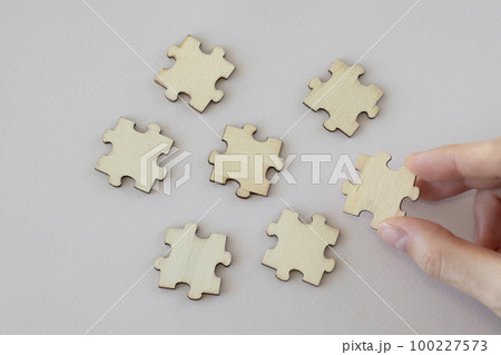 A woman's hand holds a wooden puzzle next to others scattered on a beige background. Mock Up 100227573