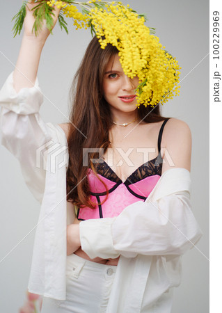 a beautiful gentle woman in a pink top and a white suit with a branch of mimosa. 100229969