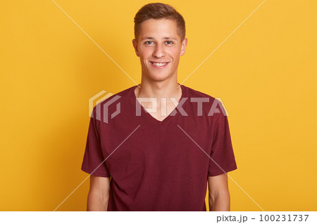 Close up portrait of smiling handsome man with blond hair, wearing in burgunde casual t shirt, standing and looking at camera, isolated on yellow studio background. Copy space for avertismant. Close up portrait of smiling handsome man with blond hair, wearing in burgunde casual t shirt, standing and looking at camera, isolated on yellow studio background. Copy space for avertismant. 100231737