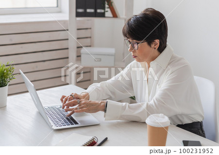 Attractive mature business woman working on laptop in her workstation - manager and office concept 100231952