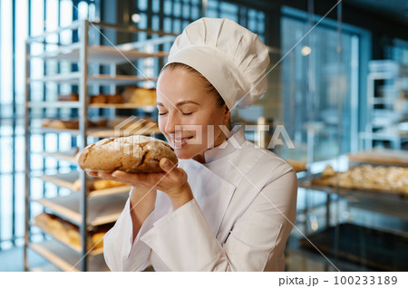 Young female baker smelling fresh bread over modern bakery background Young female baker smelling fresh bread over modern bakery background 100233189