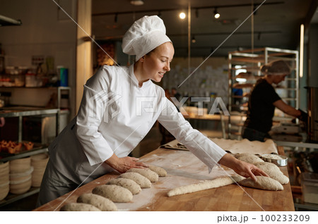 Woman baker forming bread loaves from raw dough at professional kitchen 100233209