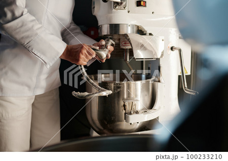 Female baker working in professional kitchen with dough mixer at bakery Female baker working in professional kitchen with dough mixer at bakery 100233210
