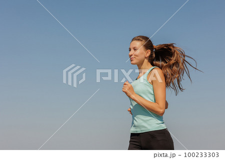portrait of sporty woman jogging in morning on ocean. young confident woman runs 100233303