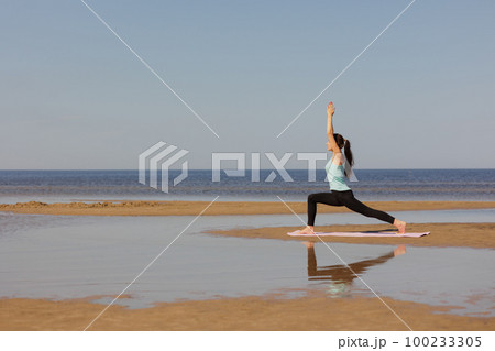 yoga, Warrior Pose, sporty woman does a warm-up on seashore in morning. 100233305