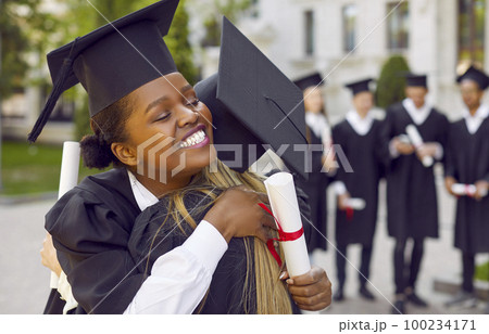 Happy African American student girl hugging her university friend on graduation day Happy African American student girl hugging her university friend on graduation day 100234171