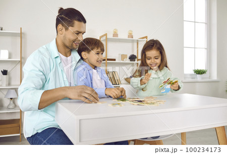 Father playing with his two kids in a puzzle in the living room at home. Father playing with his two kids in a puzzle in the living room at home. 100234173