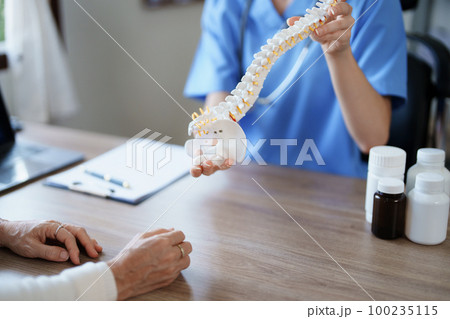 Portrait of a female doctor talking to an elderly patient about herniated disc deterioration from long hours of work 100235115