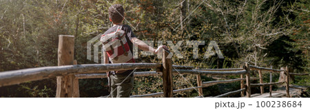 Rear on man traveler with backpack standing on bridge over river in forest. Traveling concept. 100238684