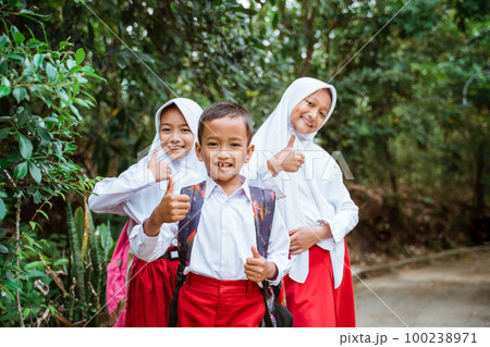 three elementary students standing at the side of country road with thumbs up three elementary students standing at the side of country road with thumbs up 100238971