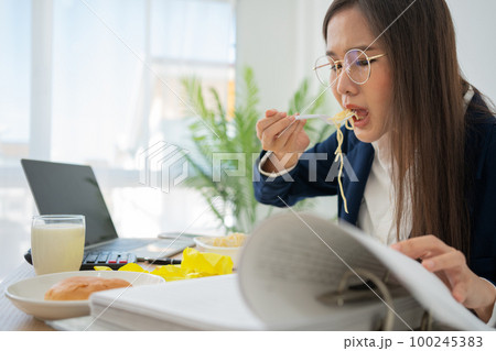Busy and tired businesswoman eating spaghetti for lunch at the Desk office and working to deliver financial statements to a boss. Overworked and unhealthy for ready meals, burnout concept. Busy and tired businesswoman eating spaghetti for lunch at the Desk office and working to deliver financial statements to a boss. Overworked and unhealthy for ready meals, burnout concept. 100245383