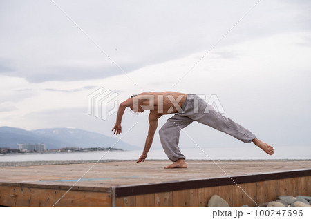 Shirtless caucasian man doing acrobatic wheel on the beach.  100247696