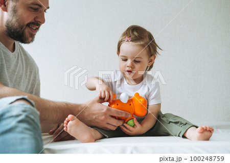 Happy father and baby girl little daughter having fun playing with toy in children room at home Happy father and baby girl little daughter having fun playing with toy in children room at home 100248759