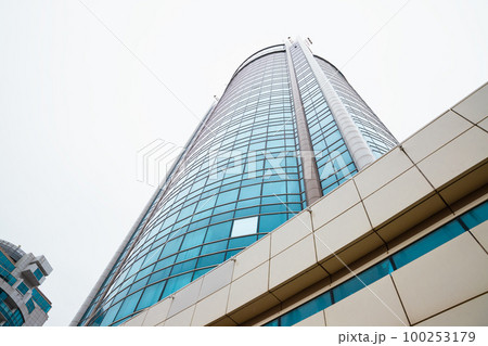 Skyscraper facade with blue glass windows on white rain clouds background. View from below, perspective. Skyscraper facade with blue glass windows on white rain clouds background. View from below, perspective. 100253179
