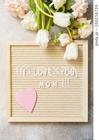 Happy Mother's Day. Letter I LOVE MOM with heart on letterboard and beautiful spring flowers. Womans day, wedding, mothers day greeting card. View from above. 100256739