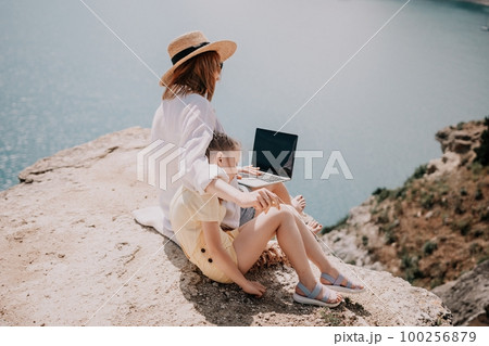 Woman sea laptop. Successful business woman working on laptop by the sea. Pretty lady typing on computer at summer day outdoors. Freelance, digital nomad, travel and holidays concept. Woman sea laptop. Successful business woman working on laptop by the sea. Pretty lady typing on computer at summer day outdoors. Freelance, digital nomad, travel and holidays concept. 100256879
