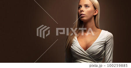 Wide studio portrait of a beautiful woman in white dress looking away 100259885