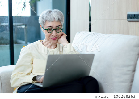 happy asian senior woman grey hair wear glasses using laptop computer sitting on couch. happy asian senior woman grey hair wear glasses using laptop computer sitting on couch. 100268263