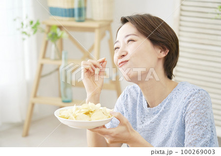 家でポテトチップスを食べる女性 100269003