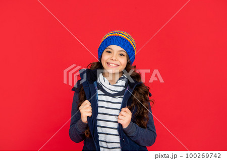 winter fashion. positive kid with curly hair in hat. teen girl on red background. 100269742