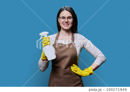 Young woman in gloves apron with organic detergent on blue background 100271949