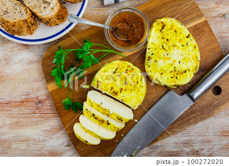 Sliced homemade cheese with spices on natural wooden board. Lithuanian traditional cheese 100272020