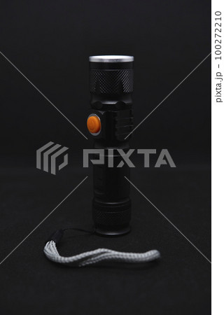 Metal black flashlight on a black background. Pocket flashlight. 100272210